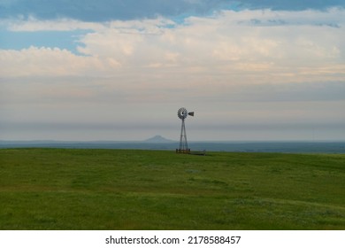 A silhouette of an old fashioned windmill stands alone along the horizon of a prairie with a butte in the background during a cloudy rainy day in North Dakota.  - Powered by Shutterstock