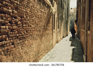 Silhouette of  old man going on narrow street in shining sun rays. (Venice, Italy) A game of light and shadow. Selective focus on the brick wall. Toned photo. - Powered by Shutterstock