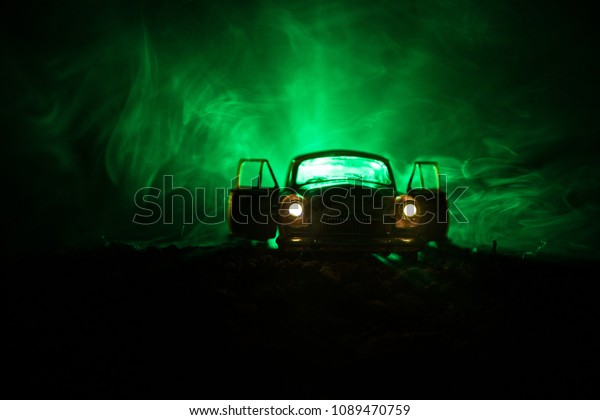 Silhouette of old vintage car\
in dark foggy toned background with glowing lights in low light, or\
silhouette of old crime car dark background. Selective\
focus