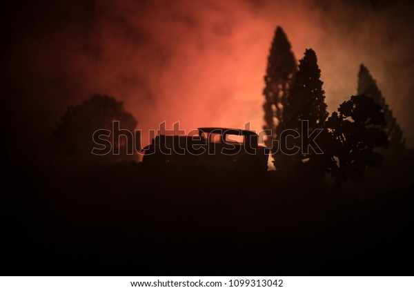 Silhouette of old vintage car in dark
foggy toned background with glowing lights in low light, or
silhouette of old car in dark forest. Selective
focus