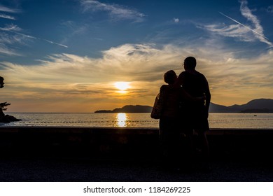 Silhouette Of Older Couple Watching Sunset On Vacation. Sun Going Into Sea With Beautiful Clouds