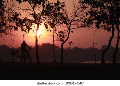 Silhouette Of The Oldman Riding A Road Bike At Sunset.