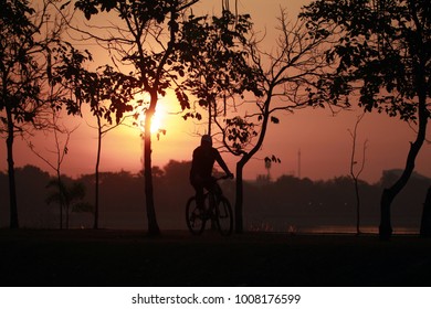 Silhouette Of The Oldman Riding A Road Bike At Sunset.