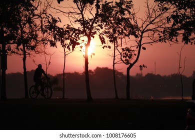 Silhouette Of The Oldman Riding A Road Bike At Sunset.