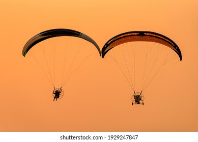 Silhouette of the Paramotor gliding and flying In the air through soft sunlight sky. Paramotor it is extreme sport