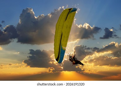 Silhouette of the Paramotor transportation control flying through soft sunlight sunset sky.