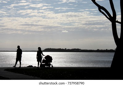 Silhouette Of Parents And Baby Carriage In Park By The Water