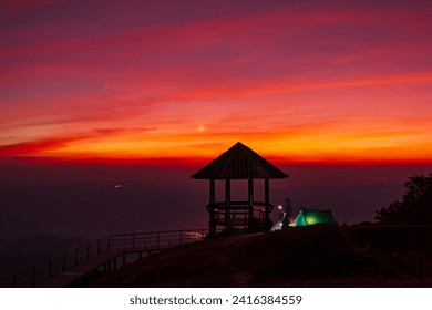 Silhouette pavilion by the hill during the dusk sky with the moon and tourists camping on the Doi Pui Co mountain in Thailand. Scenic landscape, Hiking trails, and camping in Northern Thailand - Powered by Shutterstock
