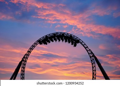 Silhouette of people having fun on a roller-coaster in an amusement park at sunset. Adrenalin concept.