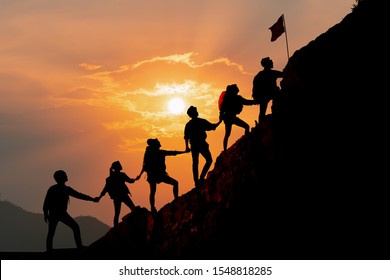 Silhouette of people helping each other hike up a mountain at sunset background. Hiking, Business, teamwork, success, help and goal concept.