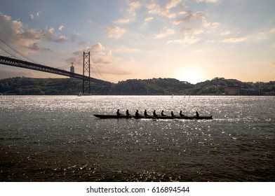 Silhouette Of People On Rowing Boat On The Sea With Suspension Bridge In The Background During Sunset. Lisbon, Portugal.