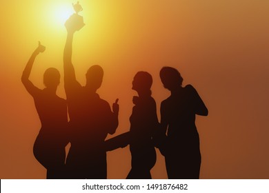 silhouette of people in team of four celebrate trophy for winning of business competition with background of sunset