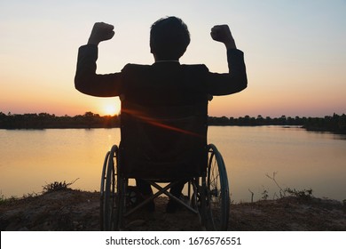 Silhouette Person With A Disability Man Seeing River Background.He Is Raise A Hand To And Sitting On Wheelchair.despair,lonely,hope.Photo Concept 	
Person With A Physical Disability And Patient.