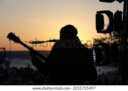 Silhouette of a person with a guitar playing at sunset outdoors
