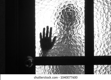 The silhouette of the person and its hand behind the door with the textured glass