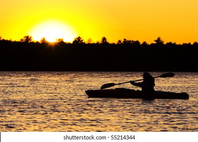 Silhouette of a person kayaking on lake at sunset.  Paddle is in mid-stroke.