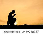 Silhouette of a person kneeling in prayer at sunset, with a golden sky background, symbolizing reflection and serenity.