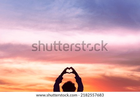 Silhouette of a person making heart with his hands with colorful sunset sky in the background. Love Your Neighbor.