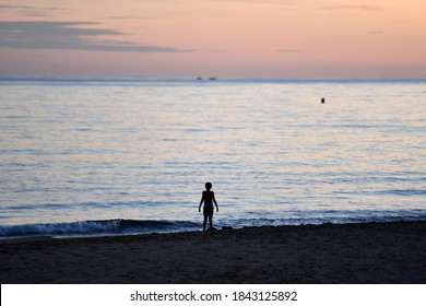 The silhouette of a person on the beach. A boy stands alone on the coast of Benidorm-Spain in the sunset while he dreamily looks out to the open sea.