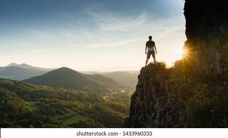 Silhouette of the person on the high rock at sunset. Satisfy hiker enjoy view. Tall man on rocky cliff watching down to landscape. Vivid and strong vignetting effect.