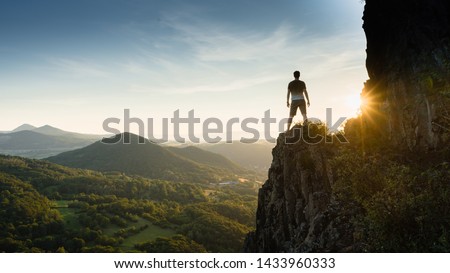 Silhouette of the person on the high rock at sunset. Satisfy hiker enjoy view. Tall man on rocky cliff watching down to landscape. Vivid and strong vignetting effect.