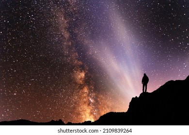 Silhouette Of A Person On The Top Of Mountain In Starry Night Sky.  Bright Milky Way Galaxy Behind Him.