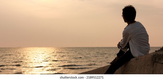 Silhouette Of Person Sitting On The Beach And Looking Beautiful Sky At Sunset