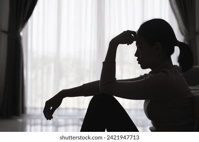 Silhouette of a person suffering from depression in the house, Depressed woman sitting alone on the Sofa feel stress, sad and worried in the dark room. person are stressed. - Powered by Shutterstock