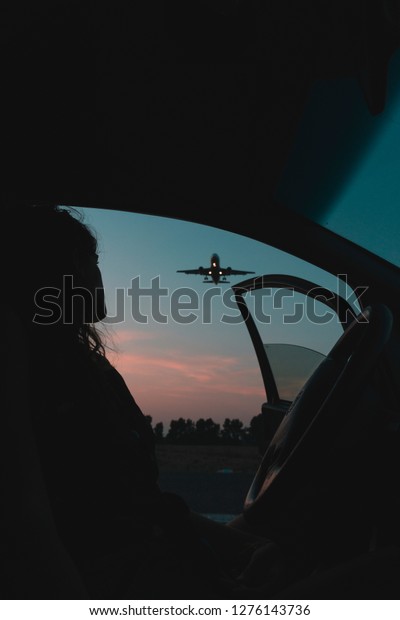 Silhouette of a person watching a landing plane in\
the car