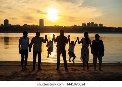 The Silhouette Photo Of Big Family With The Grandmother And Small Children On Walk On The River Bank In The Sunset Sun. Concept Of United Family And Different Generations