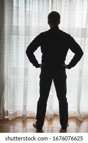 Foto de Silhouette de un hombre pensante parado encima de una gran ventana con tul y mira hacia afuera, luz de fondo