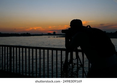 Silhouette of Photographer Capturing Sunset by the River. High quality photo - Powered by Shutterstock