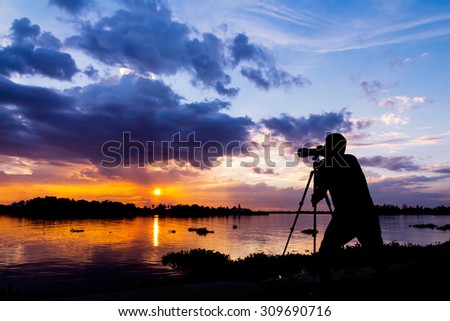 silhouette of photographer taking photo at sunset beside the river