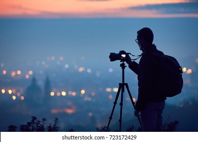 Silhouette of the photographer with tripod. Young man taking photo with his camera in the night city. Prague, Czech Republic.