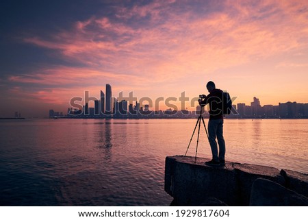 Silhouette of photographer with tripod. Young man photographing urban skyline. Abu Dhabi at dawn, United Arab Emirates