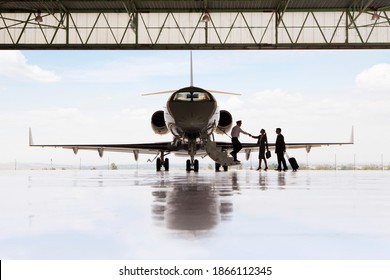 Silhouette of pilot greeting businessman and businesswoman boarding private jet in hangar - Powered by Shutterstock