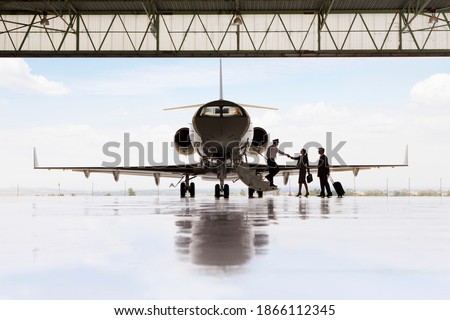 Silhouette of pilot greeting businessman and businesswoman boarding private jet in hangar