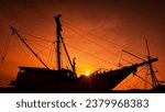 The silhouette of a Pinisi boat at red orange sunset time.