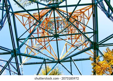 Silhouette Of A Power Line Pylon Against The Blue Sky. Transmission Of Electricity From The Power Plant To The City. Unusual Angle. Bottom View.