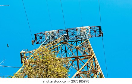 Silhouette Of A Power Line Pylon Against The Blue Sky. Transmission Of Electricity From The Power Plant To The City. Unusual Angle. Bottom View.