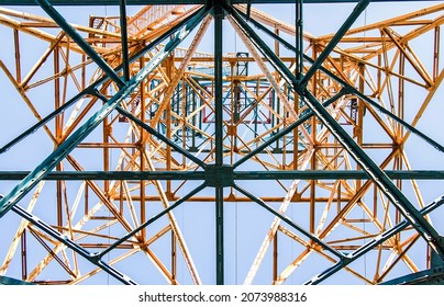 Silhouette Of A Power Line Pylon Against The Blue Sky. Transmission Of Electricity From The Power Plant To The City. Unusual Angle. Bottom View.