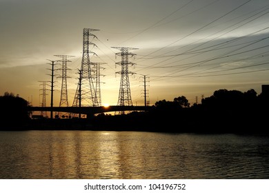 Silhouette Of Power Pylon Line From A Hydro Power Plant By A Reservoir Against A Fiery Sunset.