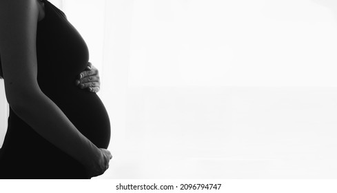 Silhouette of pregnant woman in dress at home by window touching belly. Black and white banner with copy space - Powered by Shutterstock