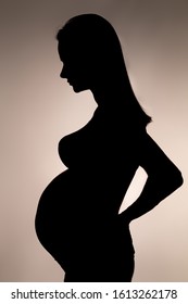 silhouette of a pregnant woman with her hair holding one hand on her lower back