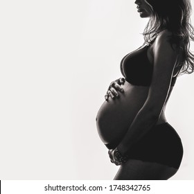 Silhouette of a pregnant woman on a white background. A mother-to-be who is expecting a baby hugs and strokes her belly. The concept of waiting, healthy and beautiful pregnancy.