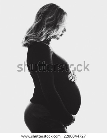 Silhouette of pregnant woman standing against white background. Side view of happy pregnant woman looking at belly. Black and white photo.