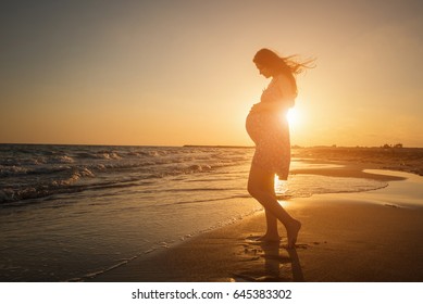 silhouette of a pregnant woman walking on the beach at sunset