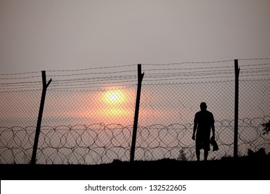 Silhouette of a prisoner behind a barbed wire fence in a concentration camp against fiery setting sun. - Powered by Shutterstock