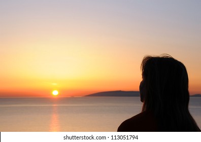 Silhouette profile of a woman looking at the sun rising from the sea