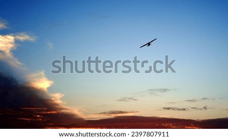 Silhouette of propeller airplane flying over dramatic orange clouds in the background
